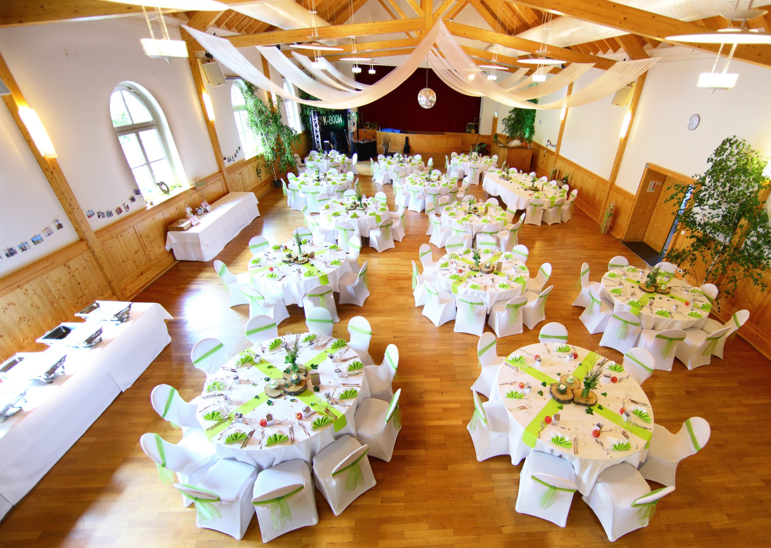 Blick von der Empore in den festlich gedeckten Saal mit runden Tischen, weißen Hussen und Holzbindern unter der Decke